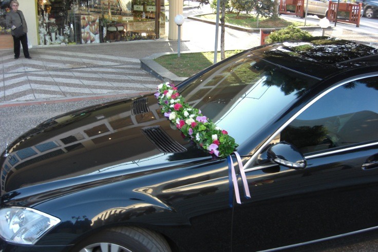 Στολισμός αυτοκίνητου γάμου με μακρόστενη κατασκευή λουλουδιών στο παρμπρίζ του αυτοκινήτου με λίλα, φούξια και λευκά λουλούδια
