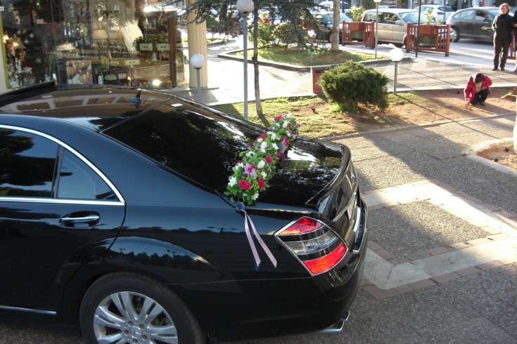 Στολισμός αυτοκίνητου γάμου με μακρόστενη κατασκευή λουλουδιών στο πίσω παρμπρίζ του αυτοκινήτου με λίλα, φούξια και λευκά λουλούδια